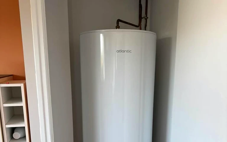 Ballon d’eau chaude installé dans un espace technique avec raccordements de plomberie visibles.