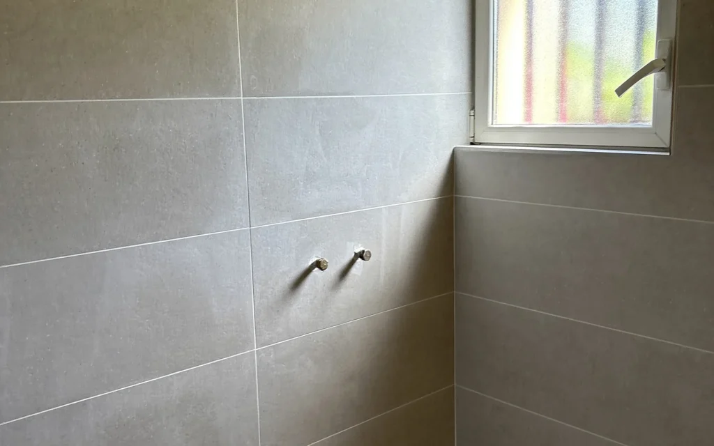 Faïence murale posée dans un espace douche à Liffré avec raccordements de plomberie visibles.