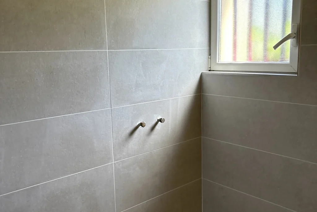 Espace douche à Liffré avec faïence grise, fenêtre et sorties de plomberie.