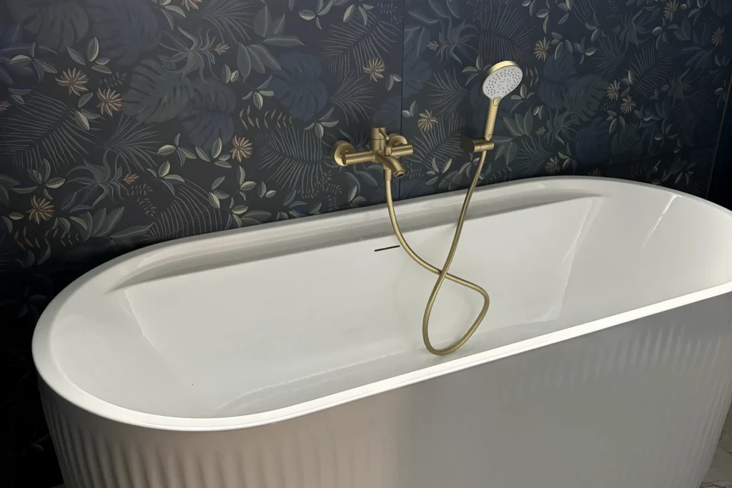 Baignoire blanche avec robinetterie dorée et faïence décorative dans une salle de bains neuve.