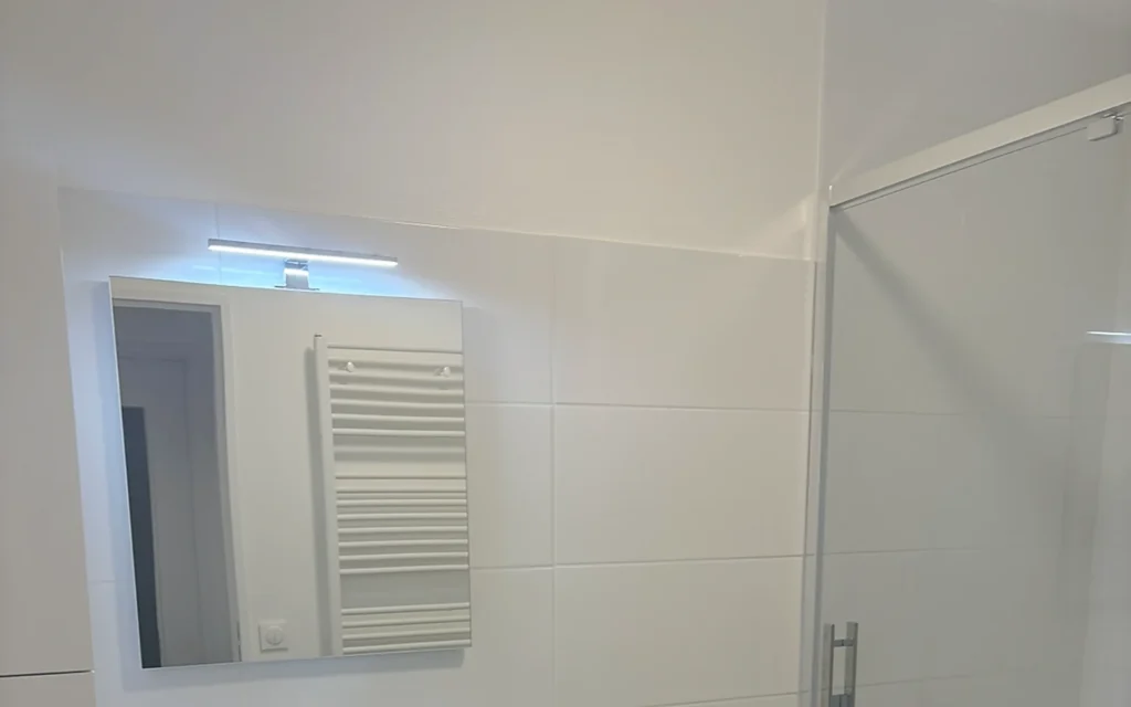Salle de bains rénovée dans le centre de Rennes avec douche vitrée, meuble vasque blanc et sol aspect bois.