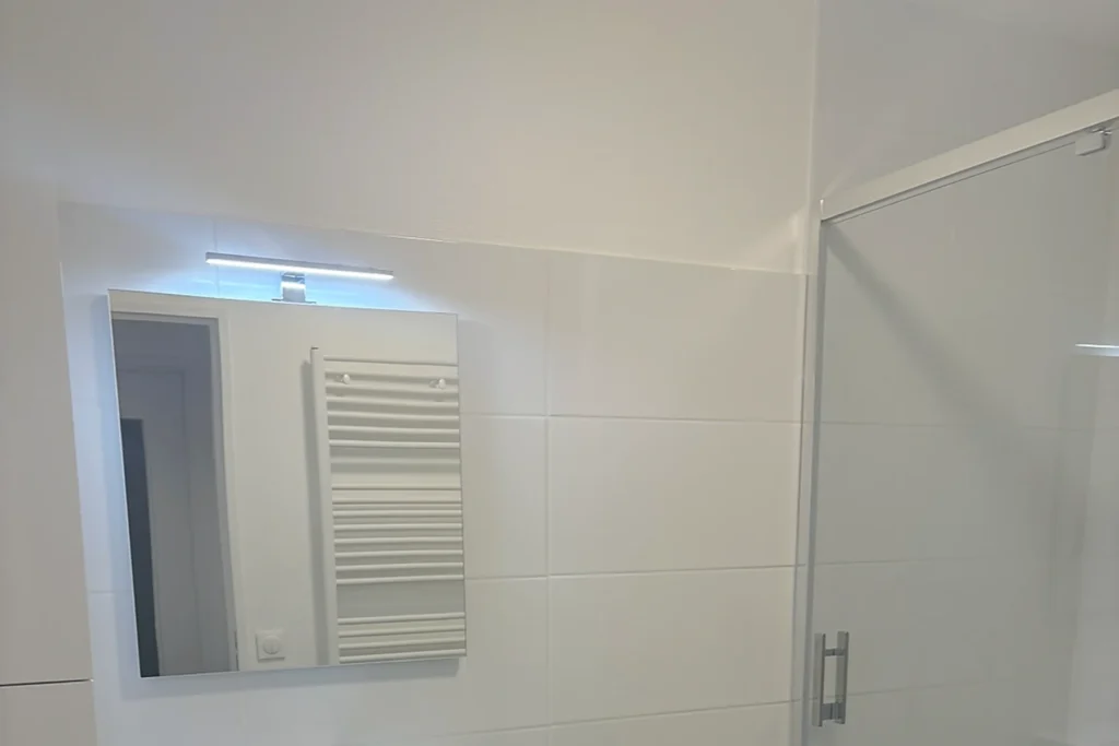 Salle de bains terminée avec douche vitrée, meuble vasque et carrelage aspect bois.