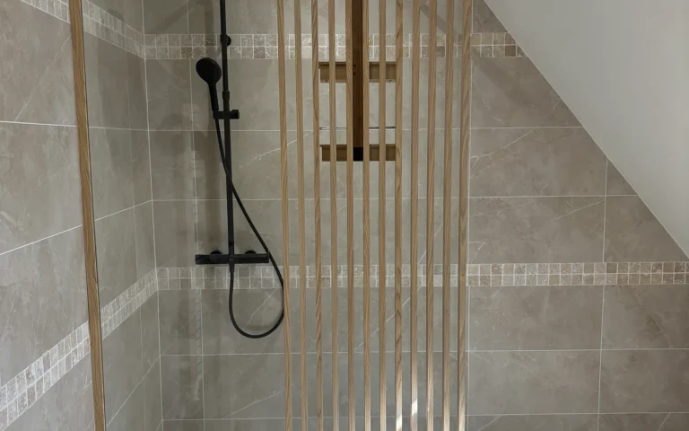 Salle de bains rénovée avec grande douche, robinetterie noire et revêtements aux tons naturels.