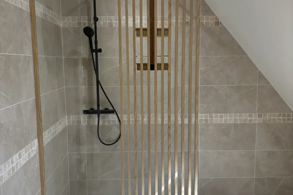 Grande douche rénovée avec paroi vitrée, faïence beige et robinetterie noire.