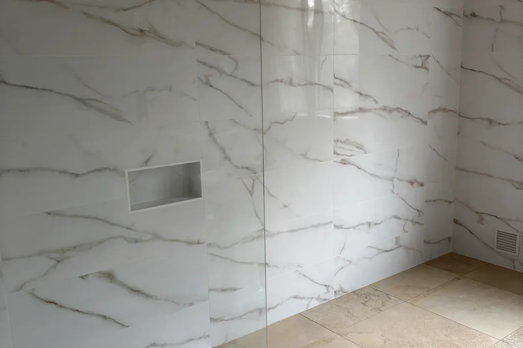 Espace douche rénové avec faïence effet marbre, niche murale et carrelage beige.