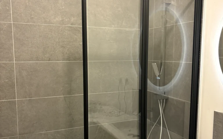 Salle de bains rénovée avec baignoire blanche, paroi vitrée noire et faïence contemporaine.