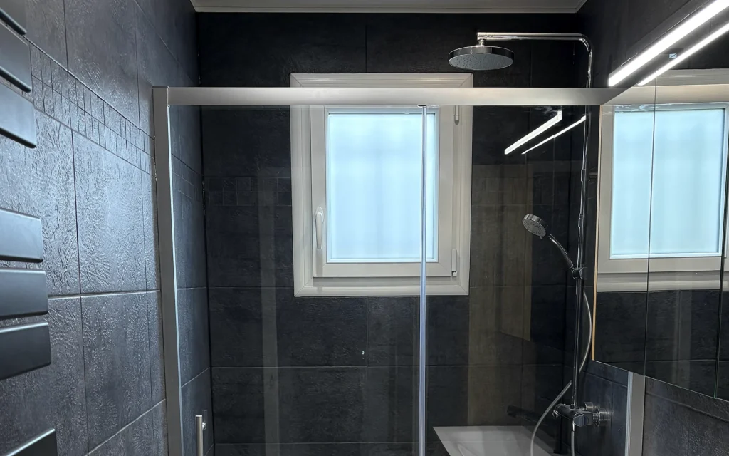 Salle de bains rénovée à Servon-sur-Vilaine avec grande douche vitrée, meuble vasque et faïence sombre.