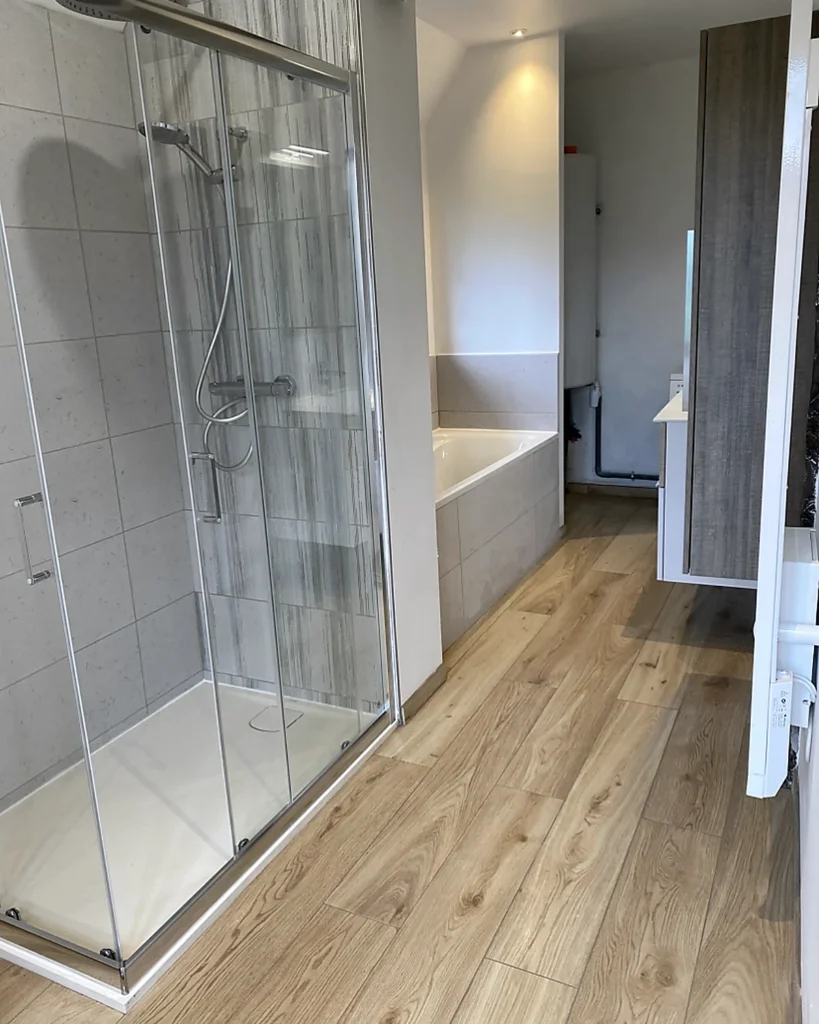 Salle de bains après rénovation à Monterfil avec douche vitrée, baignoire et faïence claire.
