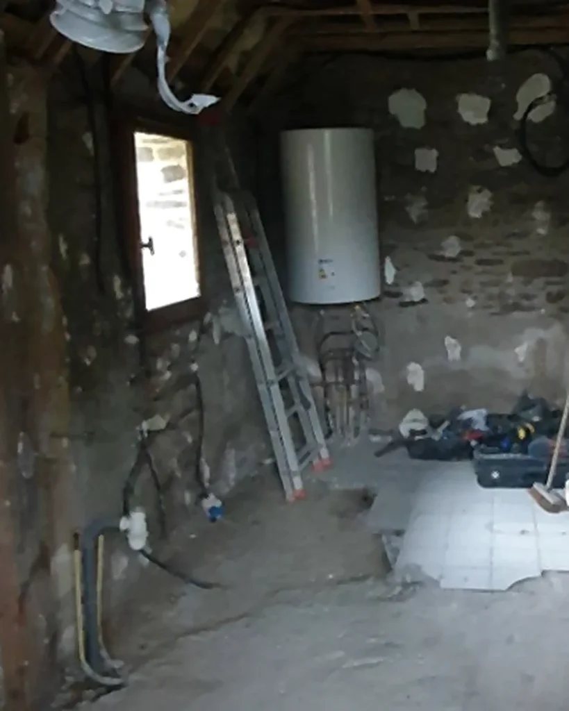 Pièce avant rénovation à Monterfil avec murs anciens, réseaux apparents et chauffe-eau.