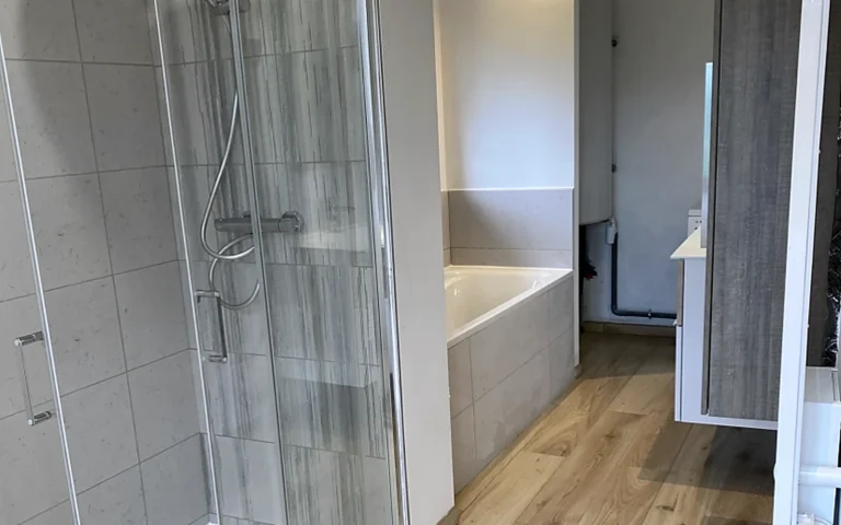 Salle de bains rénovée à Monterfil avec douche vitrée, baignoire et sol aspect bois.