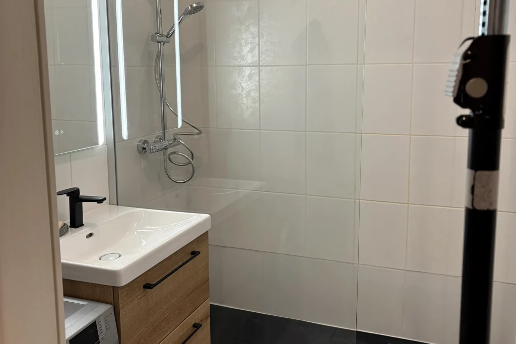 Salle de bains rénovée avec douche vitrée, robinetterie chromée et meuble vasque bois.
