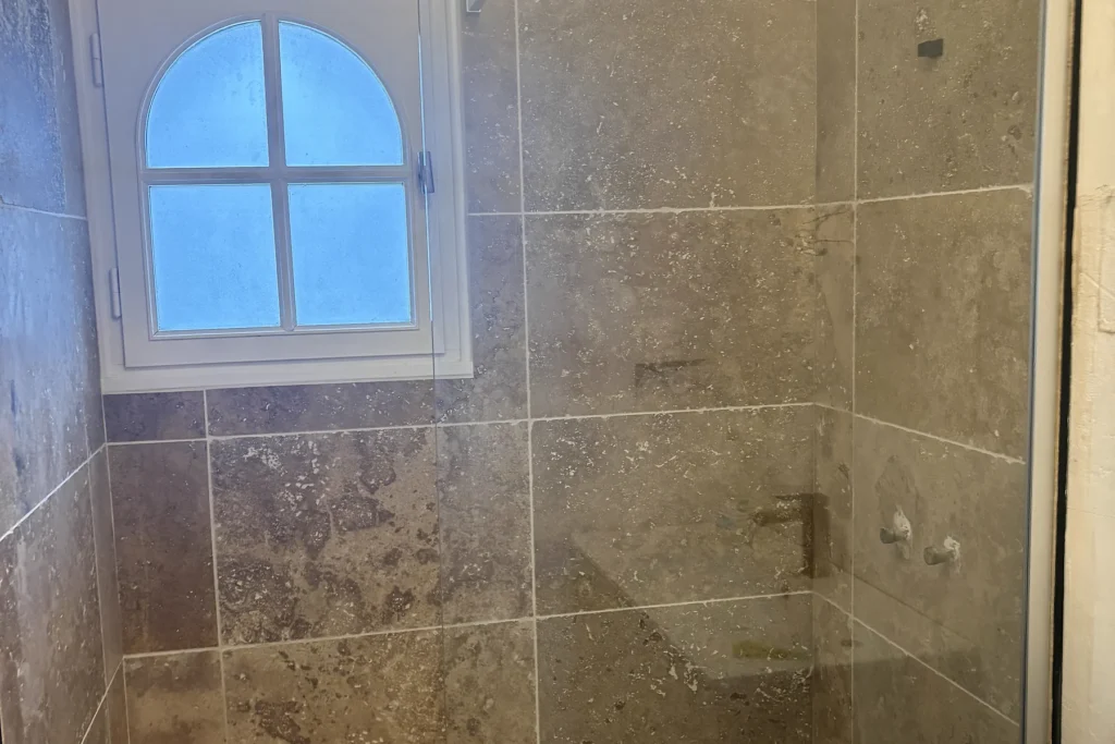 Espace douche rénové avec receveur blanc et faïence murale aux tons pierre.