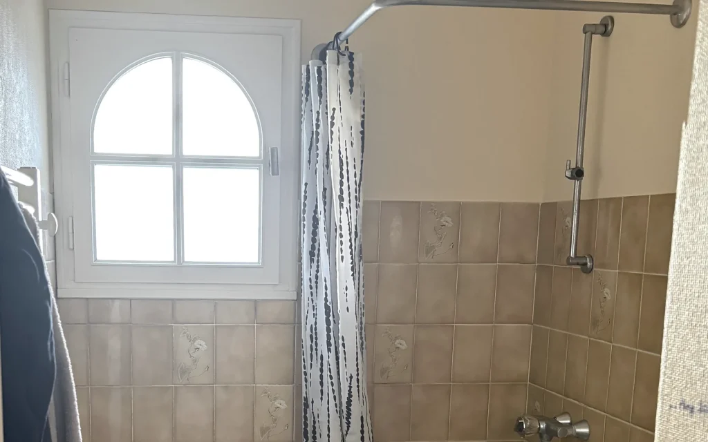 Salle de bains avant rénovation à Combourtillé avec ancien receveur, rideau et faïence beige.