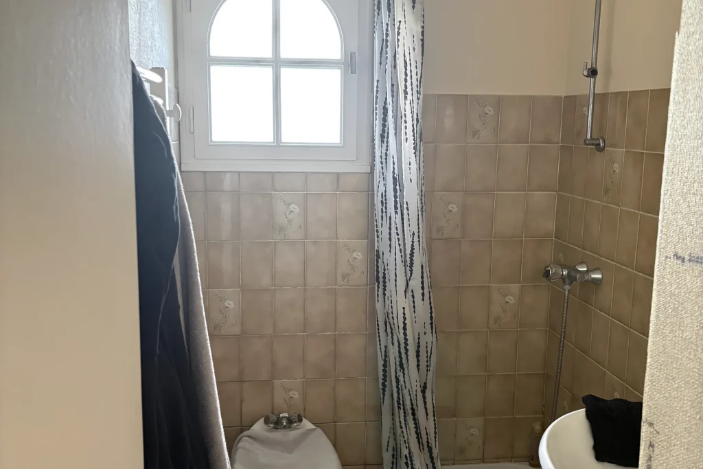 Salle de bains avant rénovation avec ancien espace douche et faïence beige.