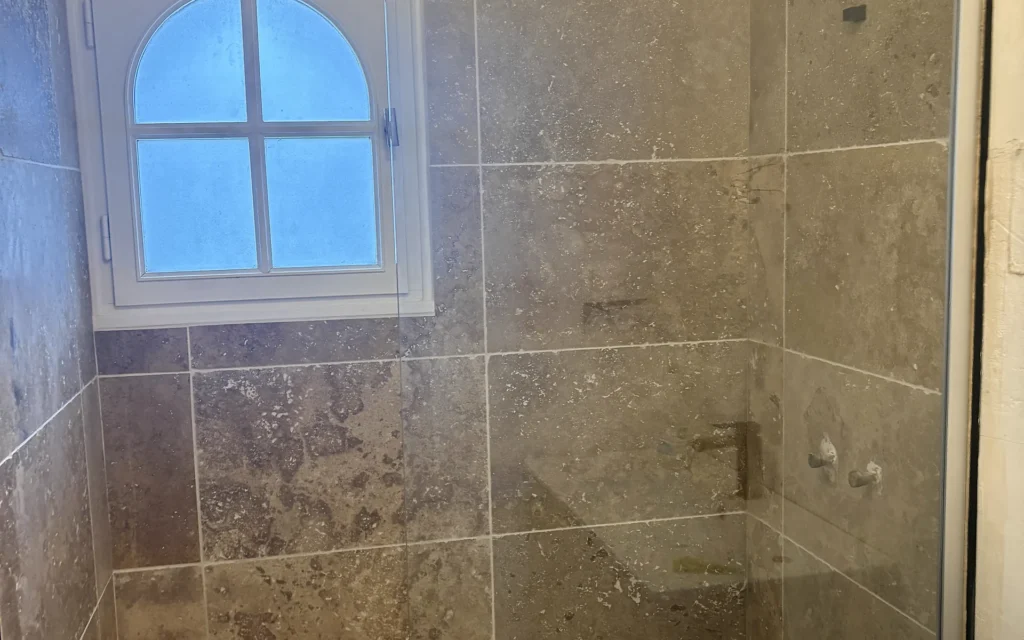 Salle de bains rénovée à Combourtillé avec receveur de douche blanc et faïence aux tons pierre.