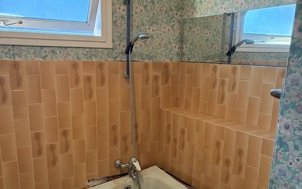 Salle de bains avant rénovation avec baignoire ancienne et revêtements datés.