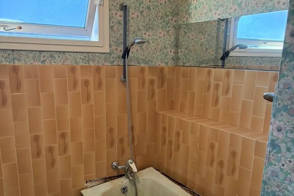 Salle de bains avant rénovation avec baignoire ancienne et revêtements datés.