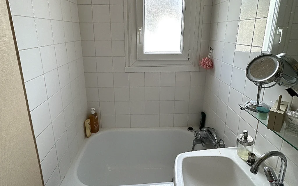 Salle de bains avant rénovation avec baignoire, faïence blanche, lavabo et fenêtre.